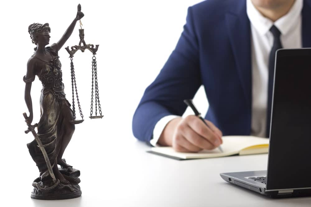 Image shows a lawyer writing at a desk with a Lady Justice statue in the foreground, concept of legal strategy and defense by a BUI charges lawyer.