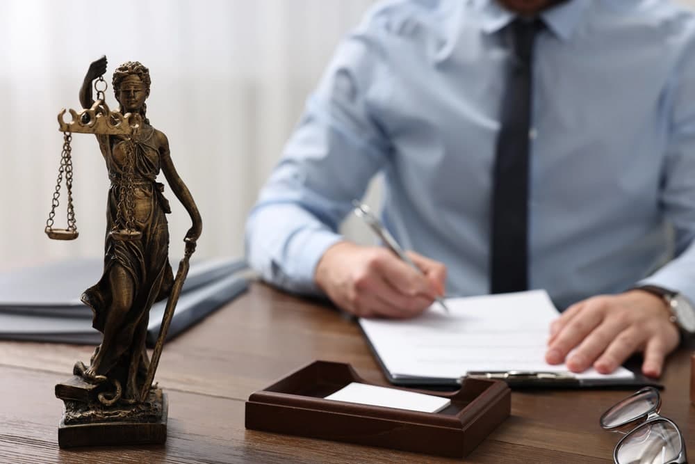 Image of a lawyer preparing case documents beside a justice statue, showing the detailed legal work performed by a burglary lawyer during client defense.