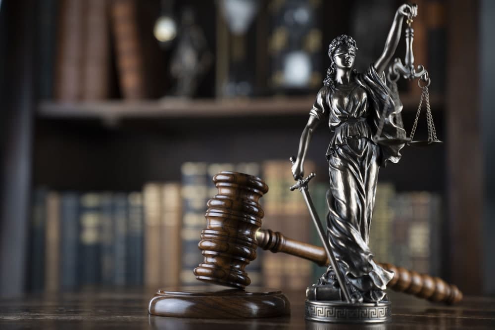 Image of a justice statue and wooden gavel in a law library, illustrating the work of a burglary lawyer handling serious property crime cases.