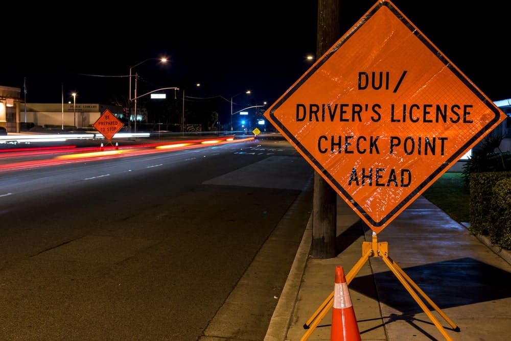 Image is of a nighttime DUI checkpoint sign on a roadway, concept of DUI lawyer guidance for stops and license checks.