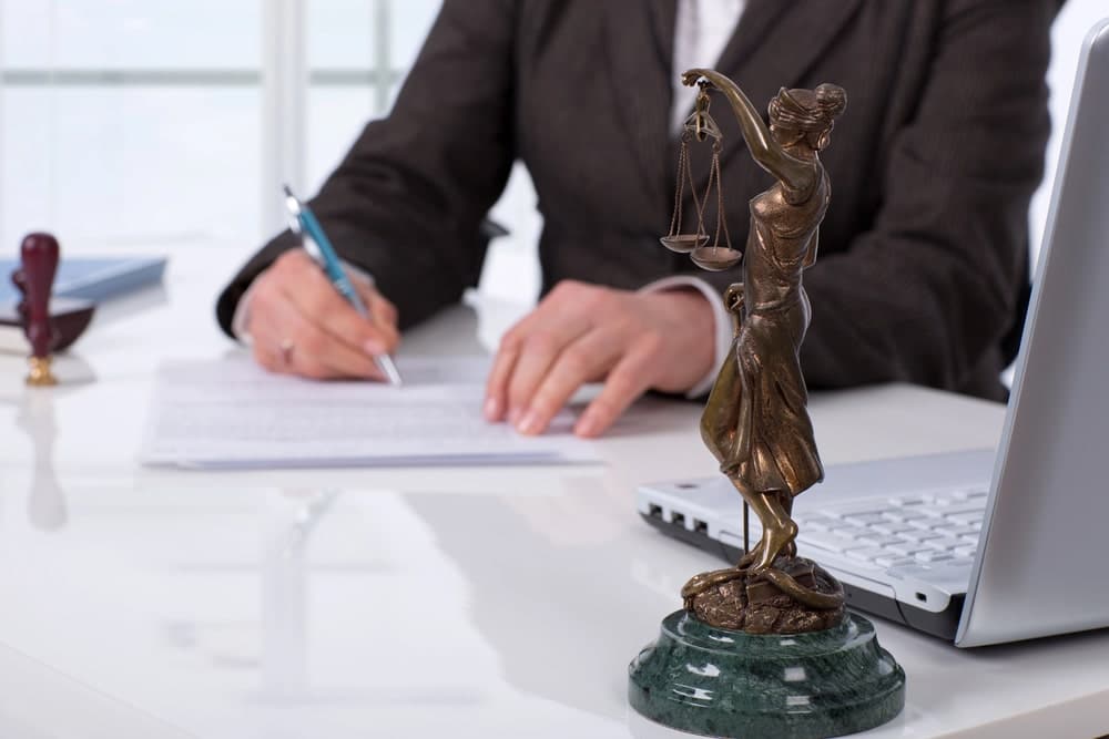 Image is of an attorney reviewing legal documents at a desk with a Lady Justice statue, concept of professional legal representation.