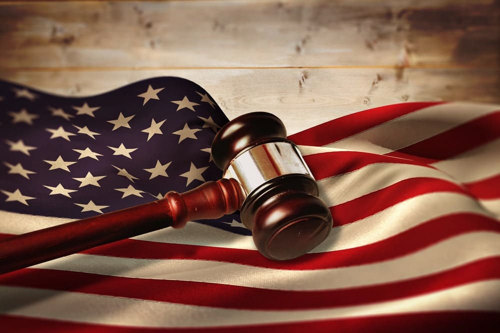Image shows a judge’s gavel resting on the United States flag, concept of legal rights and court decisions in criminal cases