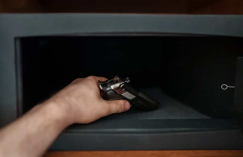 Image shows a person placing a handgun inside a security safe, illustrating firearm storage issues often discussed with a gun-weapon offenses lawyer.