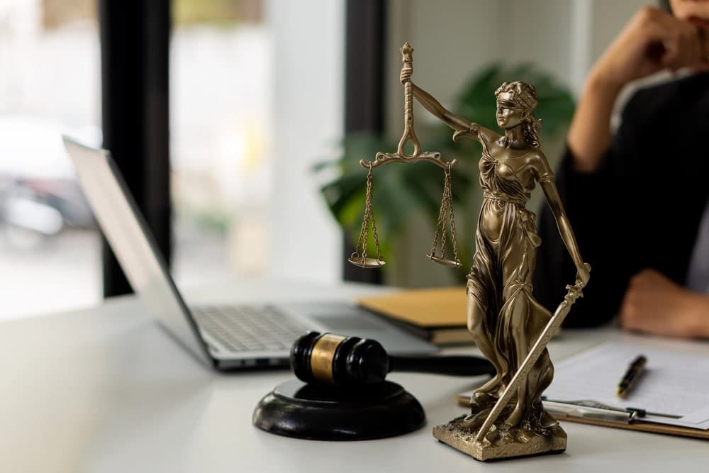 Image shows a bronze Lady Justice statue, a judge’s gavel, and legal documents on a lawyer’s desk, symbolizing legal defense and courtroom advocacy.