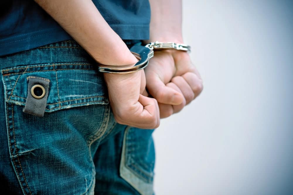 Image shows a teenager in handcuffs with hands behind the back, illustrating situations where a juvenile crimes lawyer may be needed.