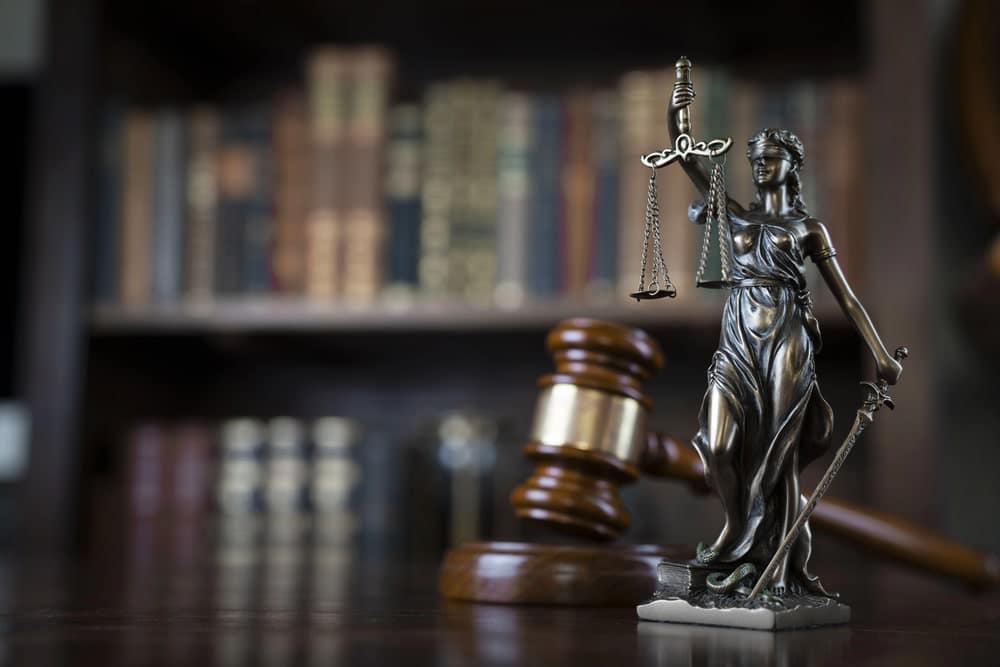 Image is of a justice statue and gavel in a law library, concept of attorneys who defend sexual criminal charges.