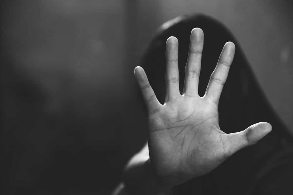 Image shows a person raising a hand in a protective gesture, concept of reporting sexual violence and seeking legal protection.