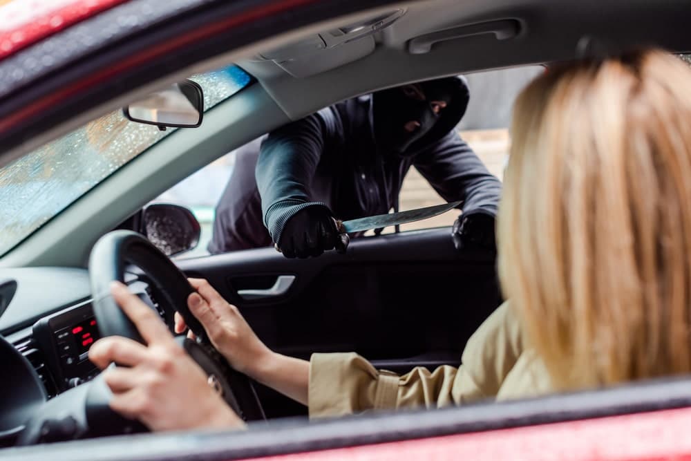Image shows a masked person holding a knife toward a driver during a carjacking, illustrating how a theft lawyer handles cases involving threats and force.