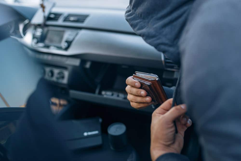Image shows a person taking a wallet from a car interior, demonstrating a real-world scenario where a theft lawyer may be needed to address property crimes.