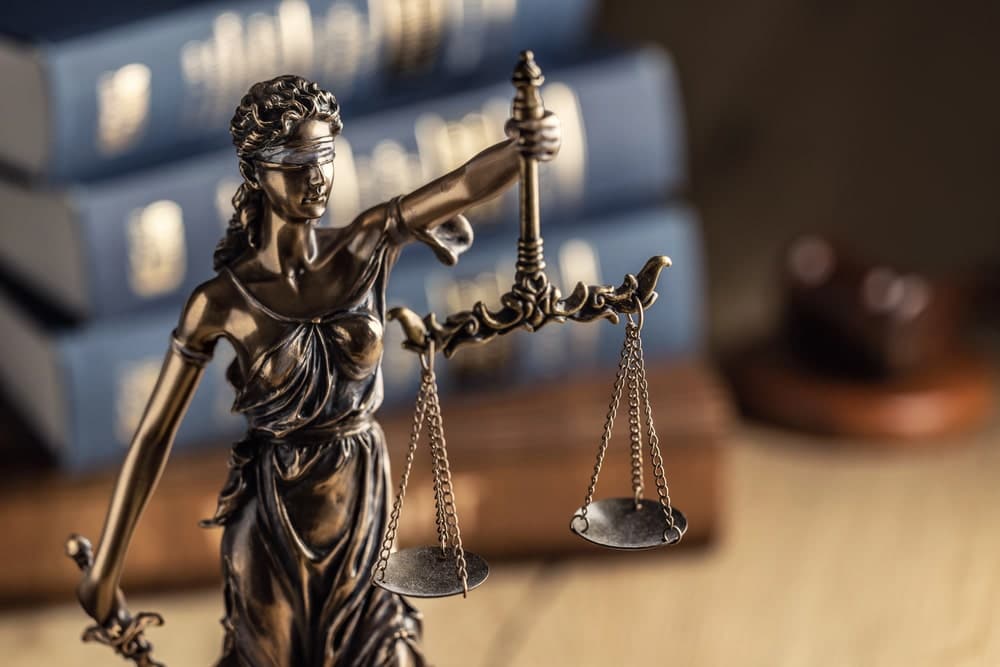 Image shows a close view of the Lady Justice statue holding balanced scales in front of law books, symbolizing fairness and legal protection in criminal cases.