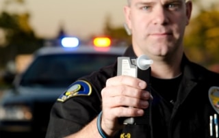 Image shows a police officer holding a breathalyzer device during a roadside stop, illustrating how DUI penalties begin.