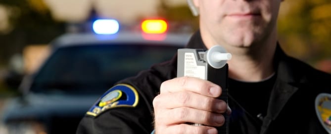 Image shows a police officer holding a breathalyzer device during a roadside stop, illustrating how DUI penalties begin.