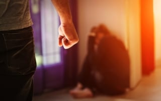 Image is of a man standing with a clenched fist while a woman sits against the wall, representing situations that may lead to a domestic violence arrest in Lebanon.