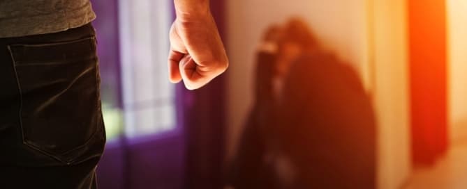 Image is of a man standing with a clenched fist while a woman sits against the wall, representing situations that may lead to a domestic violence arrest in Lebanon.