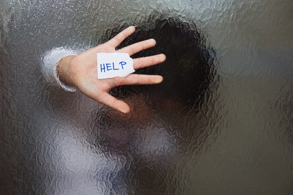 Image is of a person pressing a hand with a help note against frosted glass, symbolizing the need for protection and support after a domestic violence arrest in Lebanon.