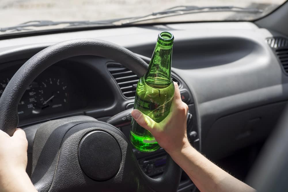 Image is of a driver holding an alcohol bottle while seated behind the steering wheel, concept of impaired driving leading to a DUI arrest in Lebanon