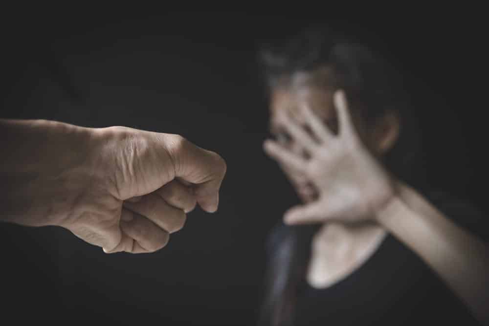 Image is of a raised fist approaching a person covering their face, representing fear and the serious impact of domestic violence charges in a personal conflict.