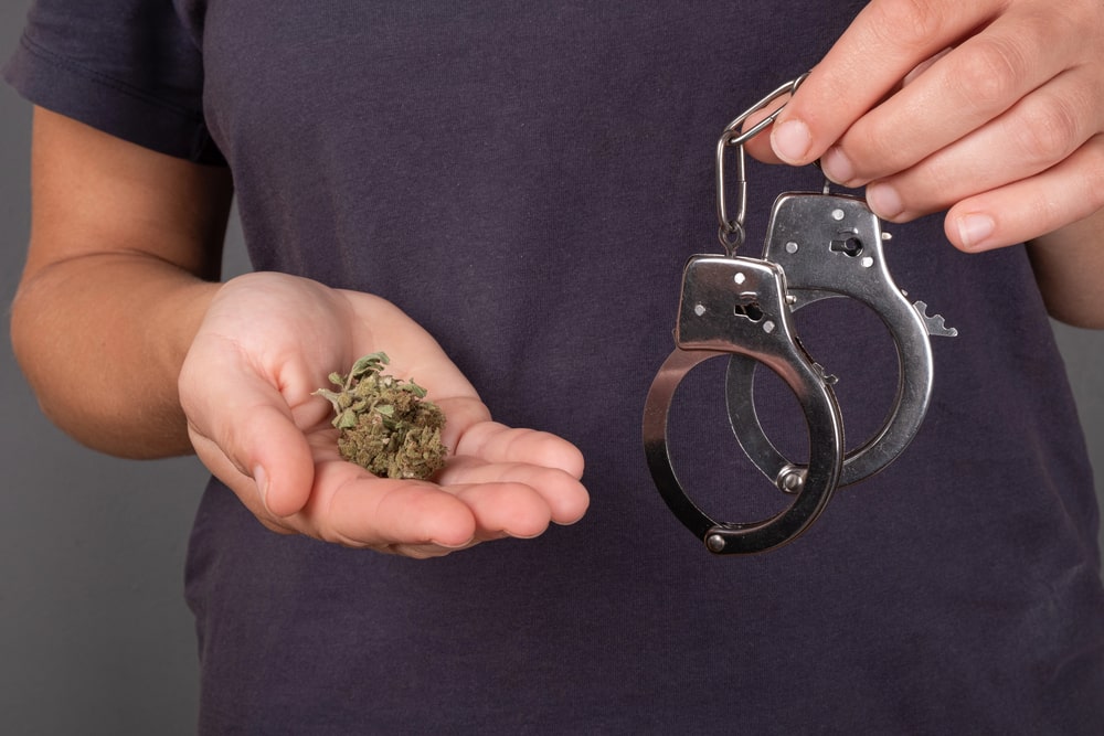 Image is of a person holding marijuana in one hand and police handcuffs in the other, illustrating Tennessee drug possession penalties and potential criminal consequences.