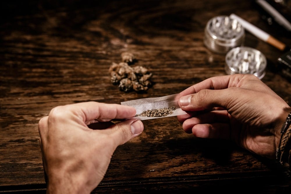 Image is of hands preparing marijuana on rolling paper on a wooden surface, concept of Tennessee drug possession penalties and unlawful controlled substance possession.