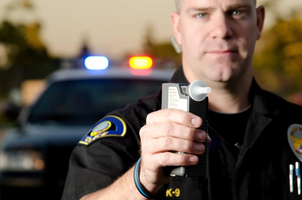 Image is of a police officer holding a breathalyzer device during a traffic stop, concept of a breath test in Tennessee
