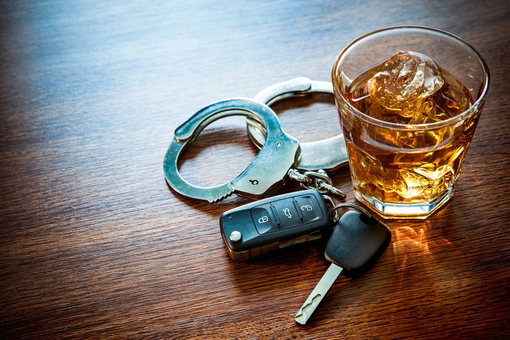 Image is of a whiskey glass beside car keys and handcuffs on a table, illustrating how DUIs affect penalties in repeat drunk driving cases.
