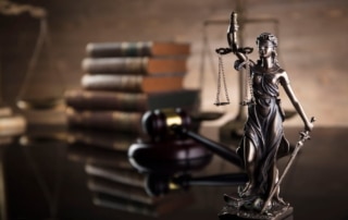 Image is of a Lady Justice statue with scales and gavel beside legal books, representing sexual assault penalties and how courts review serious criminal charges