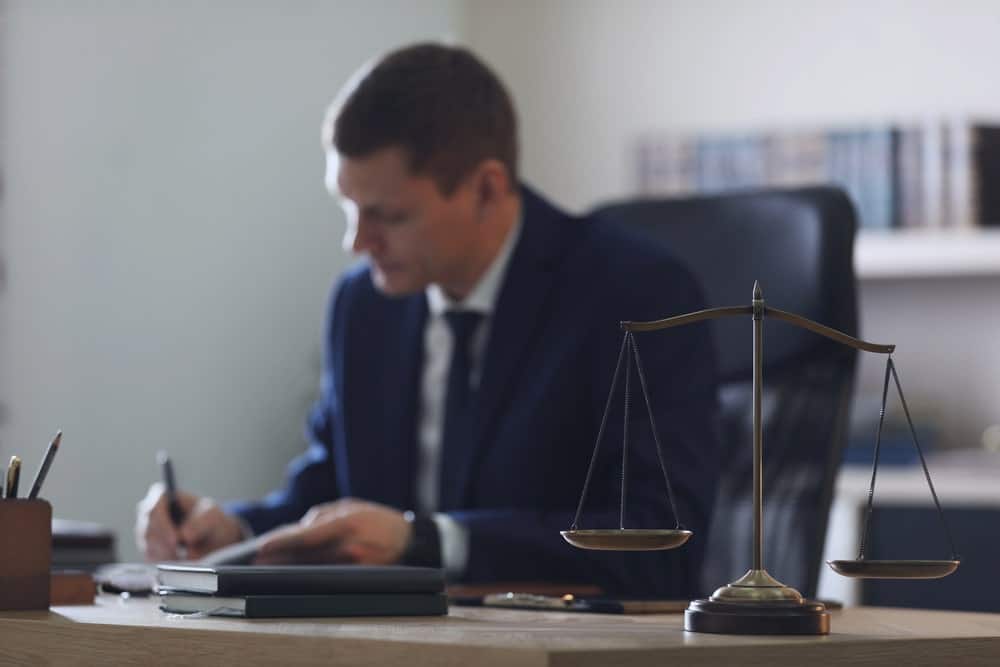 Image is of a lawyer reviewing documents at a desk with scales of justice in focus, concept of legal evaluation of sexual assault penalties in Tennessee
